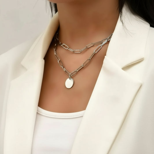 Silver chain necklace with a round pendant on a person wearing a white outfit.