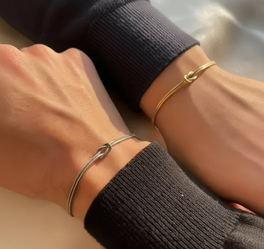 Two wrists with gold and silver bracelets on a neutral background