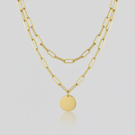 Gold chain necklace with a pendant on a person wearing a white blazer.