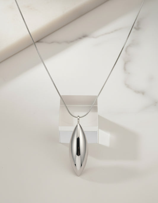 Silver necklace with a pendant being held by a hand against a blurred background